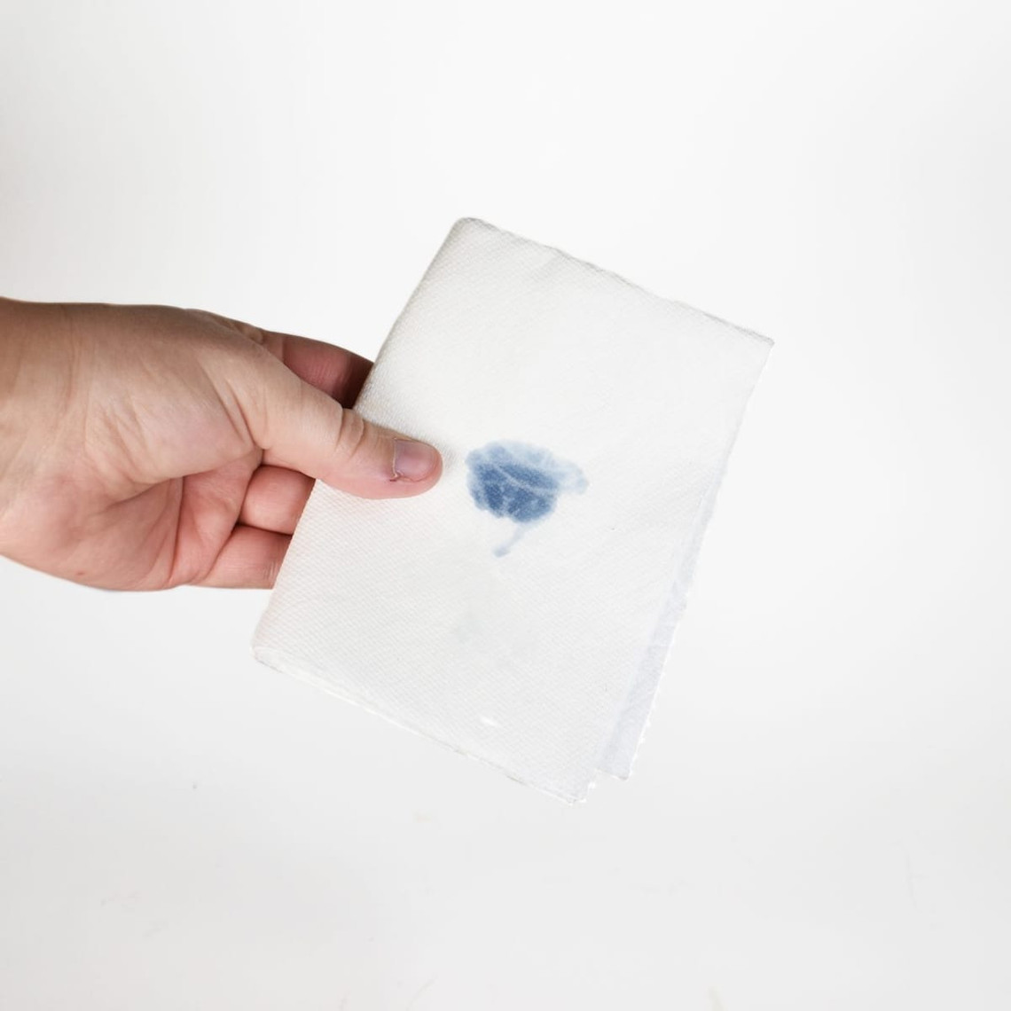 Hand holding a folded white paper towel marked with a blue wax color-test spot