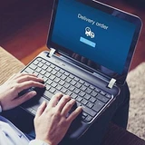 Person typing on a laptop showing a blue Delivery order tracking screen