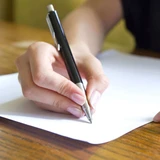 Close-up of a hand writing on a blank white sheet of paper with a black pen