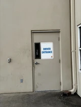Gray metal door on a beige warehouse wall marked with a Driver Entrance sign