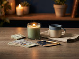 lit green candle, blue mug, fanned hundred-dollar bills, and a gold pen on a wooden table