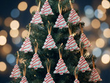 White tree-shaped freshies with red icing stripes hung by ribbon on a Christmas tree, golden bokeh lights behind
