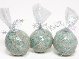 Three round bath bombs speckled gray with teal flecks, wrapped in clear cellophane tied with silver star-spangled ribbon, on a white background