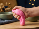 Hand squeezing a stretchy ball of bright pink slime on a wood board, cozy styled backdrop