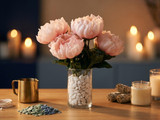 Pale pink peony bouquet in a pebble-filled glass vase beside candles and sage bundles