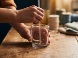 Hands centering a wick with a straw in an empty glass jar beside spools of wick