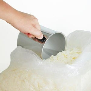 Hand scooping soy wax flakes from a plastic bag with a metal measuring cup