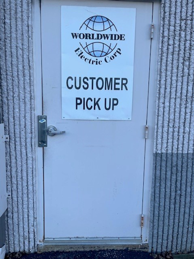 White metal door with a Worldwide Electric Corp Customer Pick Up sign