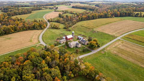 Aerial view of a Pennsylvania farmstead with a red barn and silo amid patchwork fields and autumn trees