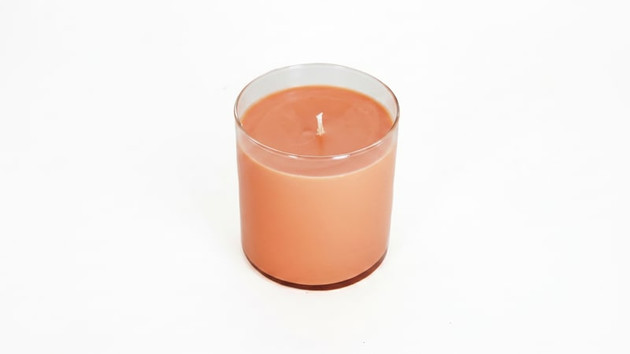 Single unlit peach-colored candle cooling in a clear glass tumbler on a white background