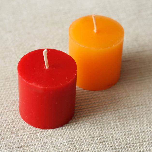 Unlit red and orange votive candles side by side on a woven beige cloth
