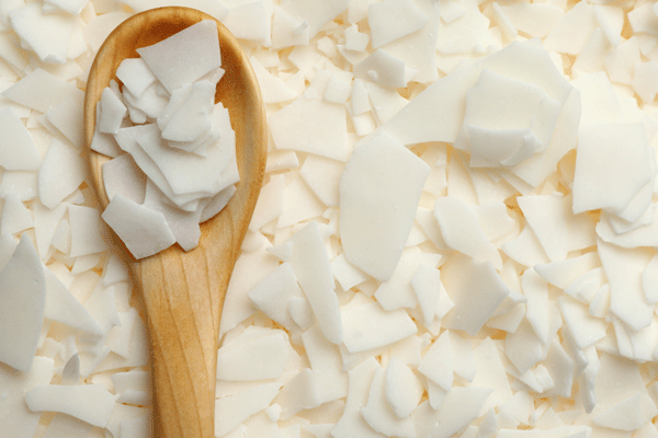 Wooden spoon scooping white soy wax flakes from a spread of loose flakes