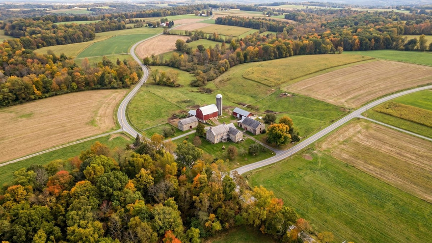 Aerial view of a Pennsylvania farmstead with a red barn and silo amid patchwork fields and autumn trees