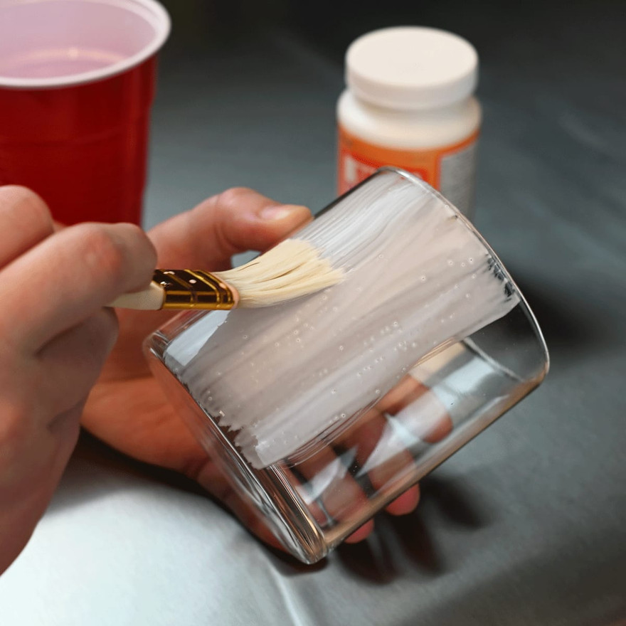 hand brushing glue onto the outside of a glass jar