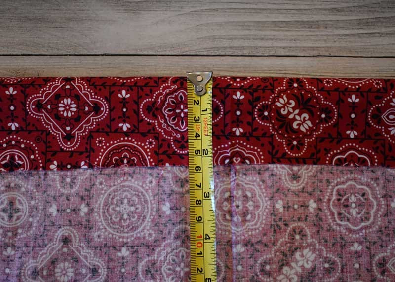 Yellow tape measure laid across folded red paisley bandana fabric on a gray wood surface