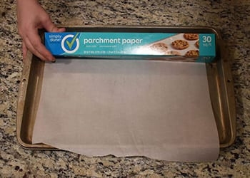 Hand holding a Simply Done parchment paper box over a parchment-lined baking sheet on granite