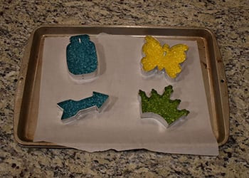 Four bead-textured freshies, blue mason jar, yellow butterfly, blue arrow, green crown, on a parchment-lined baking sheet