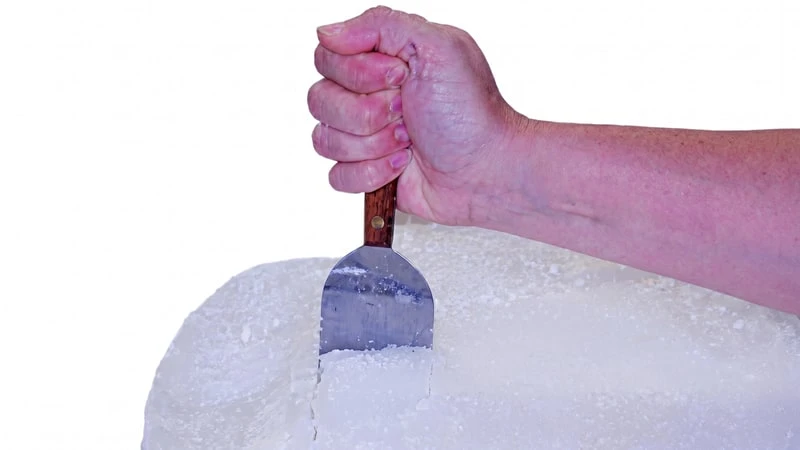 Hand pressing a wood-handled metal scraper into a block of white candle wax