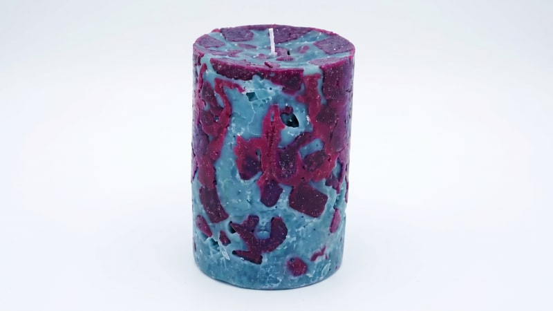 Finished pillar candle mottled with teal-blue and magenta holes from the ice technique