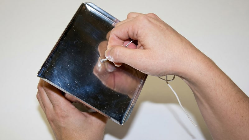 Hands threading a white wick through the base hole of a square metal mold