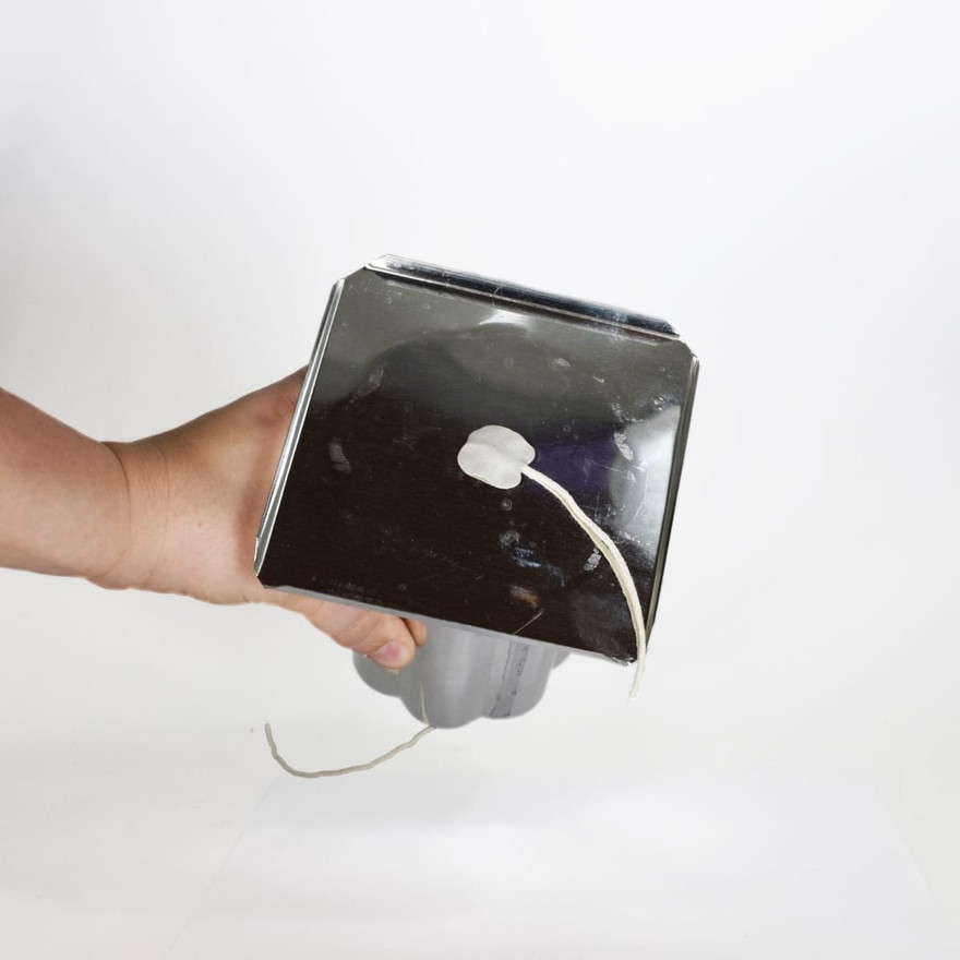 Hand holding upside-down metal pillar mold base, wick hole sealed with white mold putty