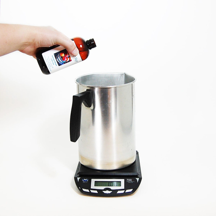Hand tipping amber Lone Star fragrance oil bottle over a steel pouring pot on a digital scale