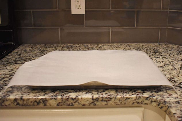 Parchment-lined baking sheet on a speckled granite counter against a gray tile backsplash