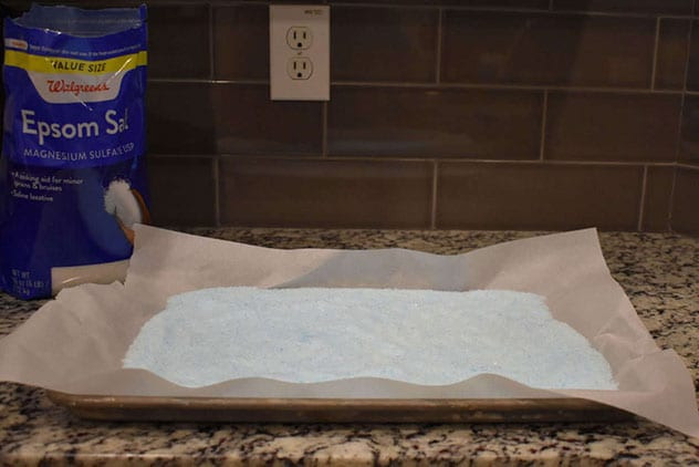 Evenly tinted pale-blue Epsom salt spread on a parchment-lined sheet beside the salt bag