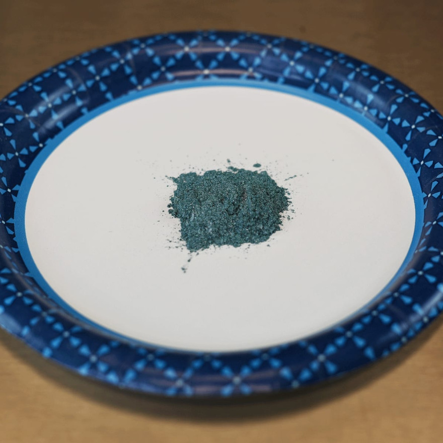 A mound of teal mica powder on a white paper plate
