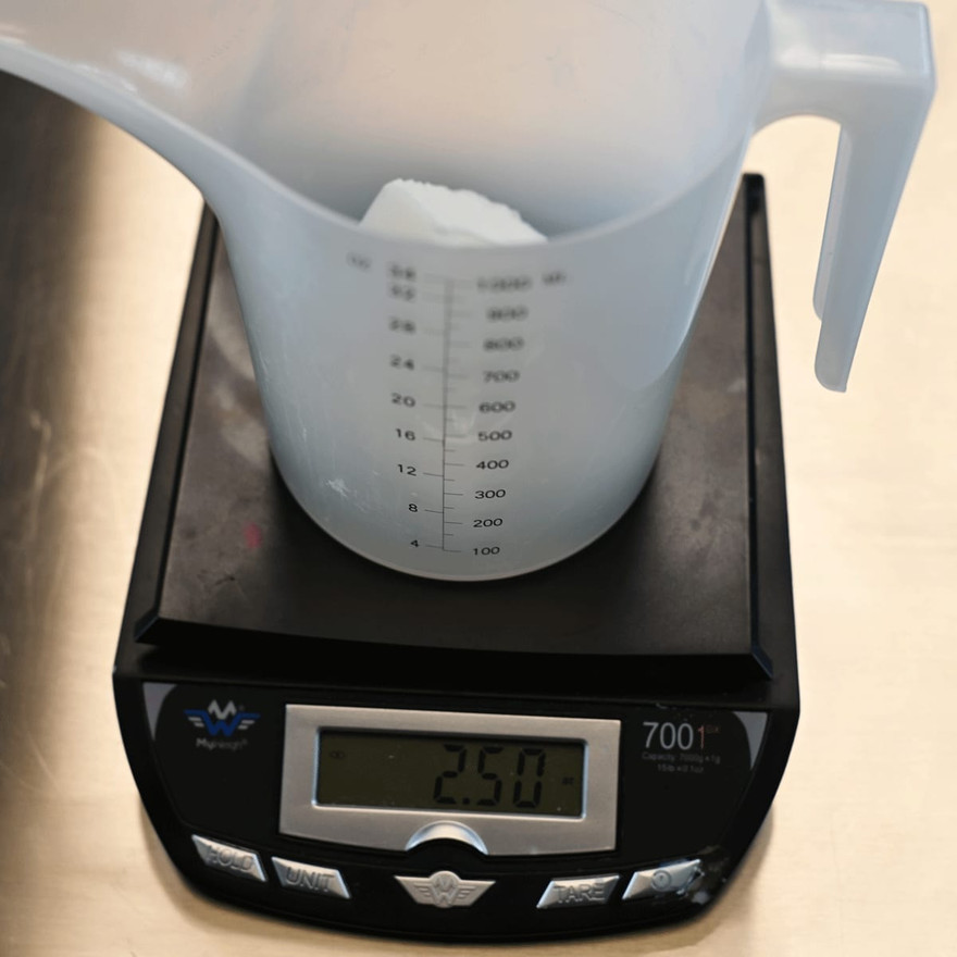 A measuring pitcher of soap base on a digital scale reading 2.50 ounces