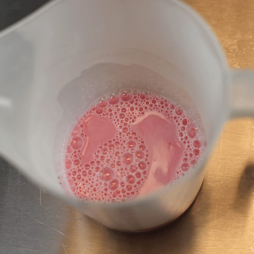 A pitcher of melted pink-tinted soap base with surface bubbles