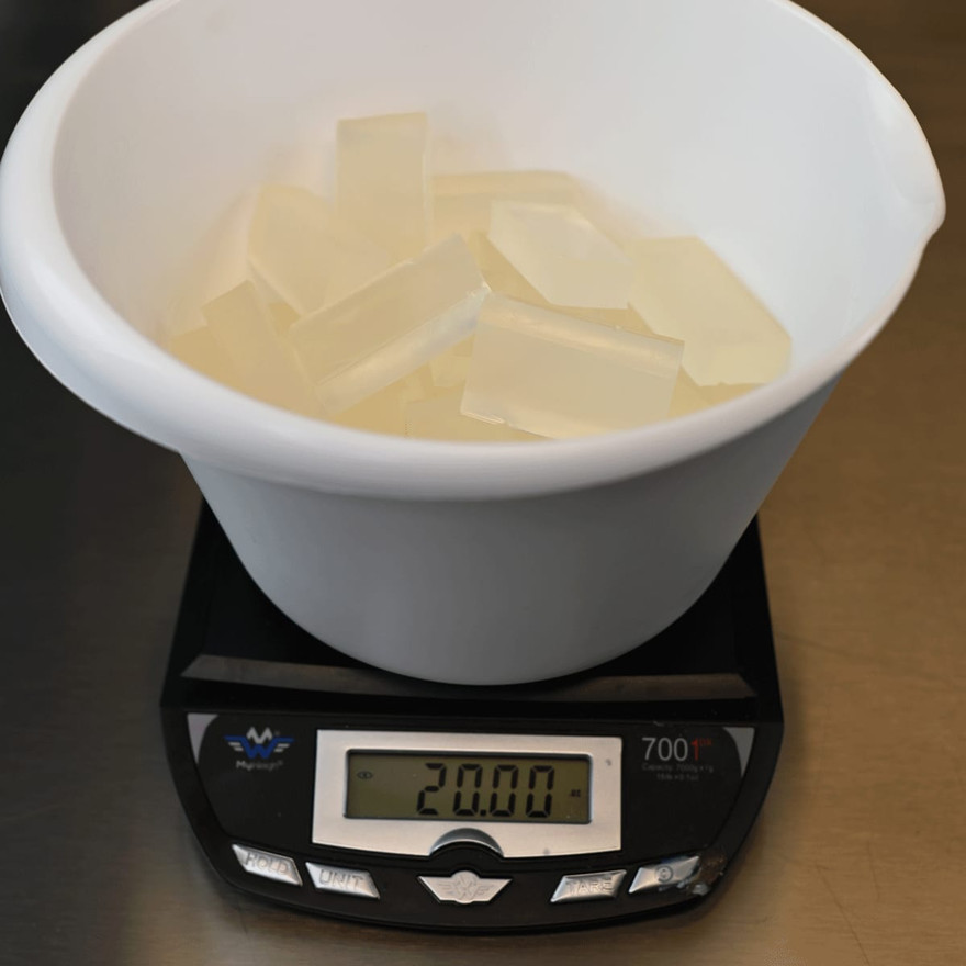 A bowl of cut clear soap base pieces on a scale reading 20 ounces