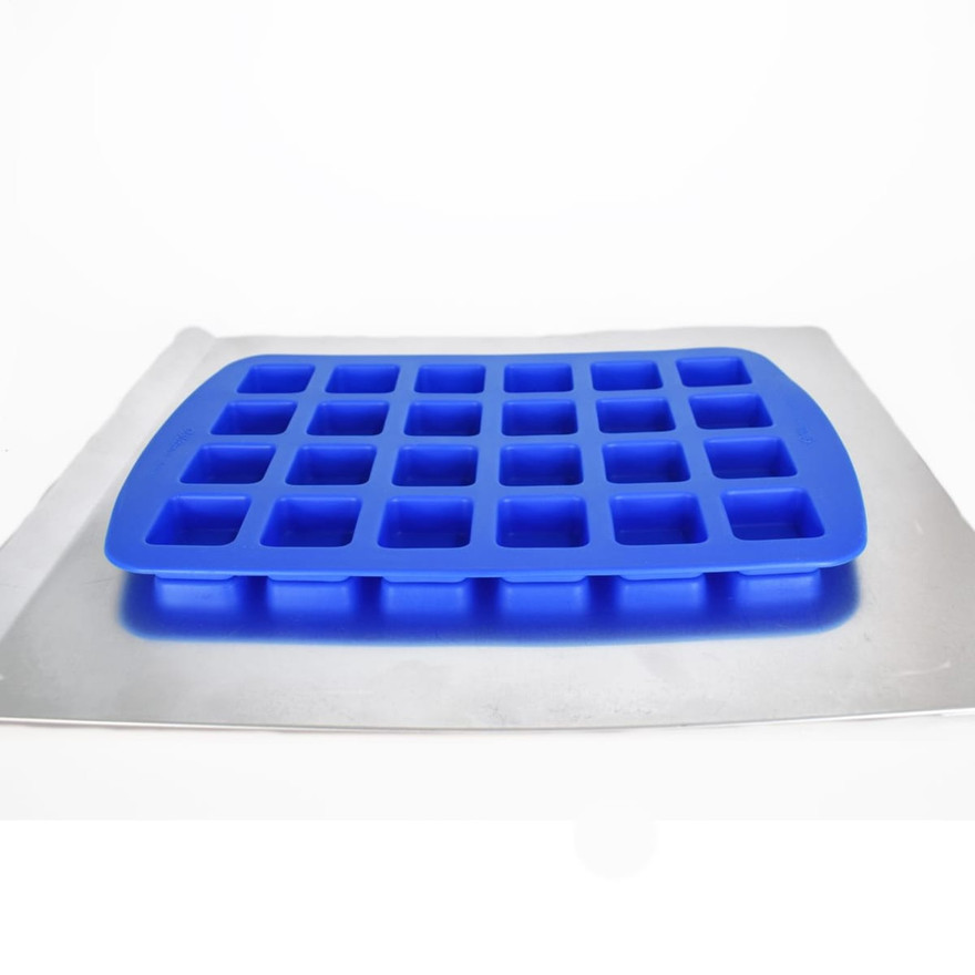 Empty blue silicone mold with 24 square cavities resting on a metal baking sheet