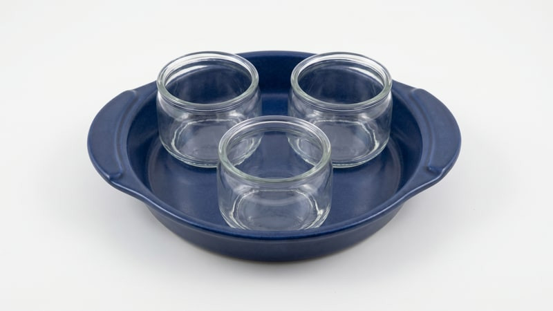 Three empty clear glass jars arranged in a navy ceramic baking dish