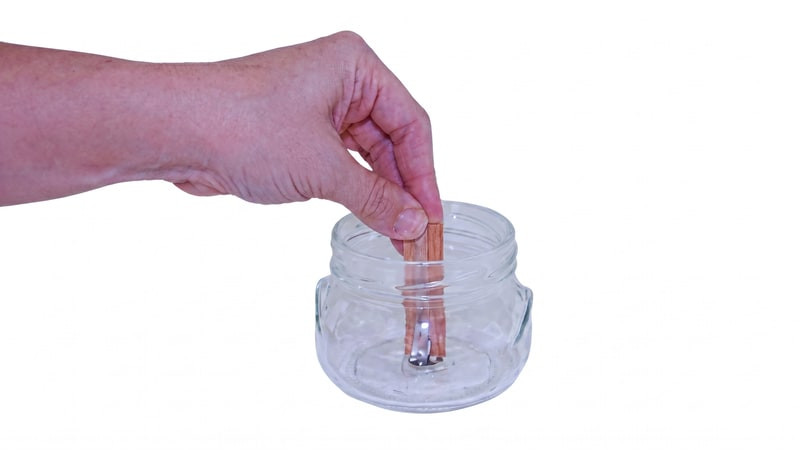 Hand setting a wooden wick in a metal tab into the center of an empty glass jar